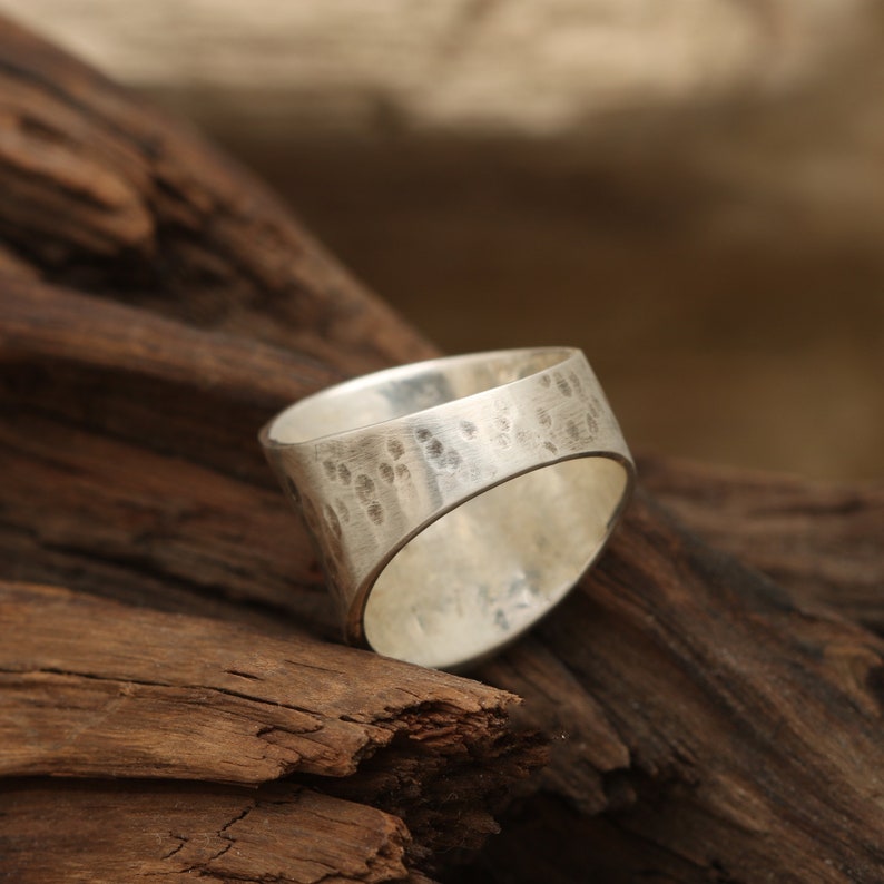 May include: A silver ring with a hammered texture. The ring is wide and has a rounded shape.