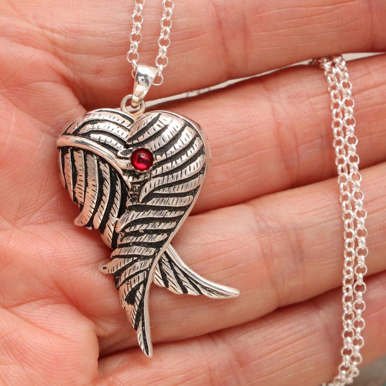 Pu&ograve; includere: Collana con ciondolo a forma di cuore in argento con una pietra preziosa rossa al centro e un design ad ala dettagliato.