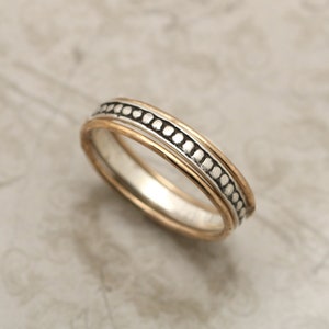 May include: A thin silver band ring with a gold band inside and a row of small silver beads around the outer edge.