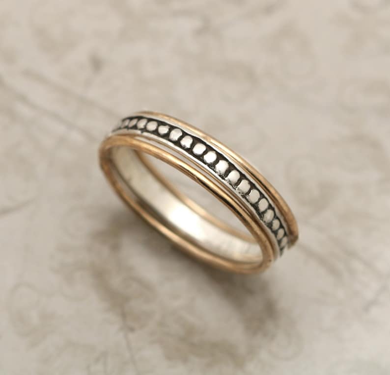 May include: A thin silver band ring with a gold band inside and a row of small silver beads around the outer edge.
