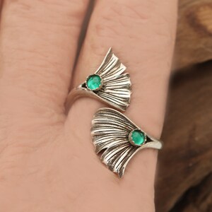 Puede incluir: Un anillo de plata con dos dise&ntilde;os de hojas de ginkgo. Cada hoja tiene una piedra preciosa verde en el centro.