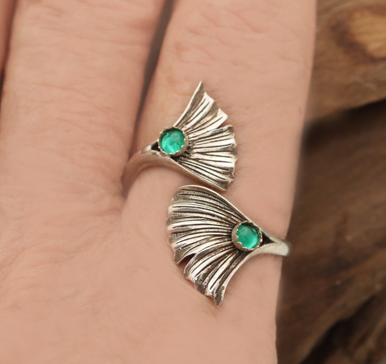 Puede incluir: Un anillo de plata con dos dise&ntilde;os de hojas de ginkgo. Cada hoja tiene una piedra preciosa verde en el centro.