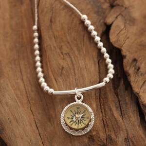 May include: A silver necklace with a compass pendant. The compass is round and has a gold face with black markings. The necklace is made of small silver beads.