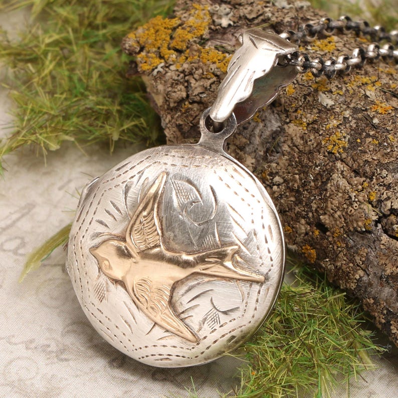 May include: Silver locket with a gold-toned swallow design. The locket has a detailed engraved pattern and a hinged opening.