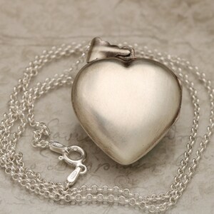 May include: A silver heart-shaped locket pendant with a chain. The locket is closed and has a smooth, polished finish.