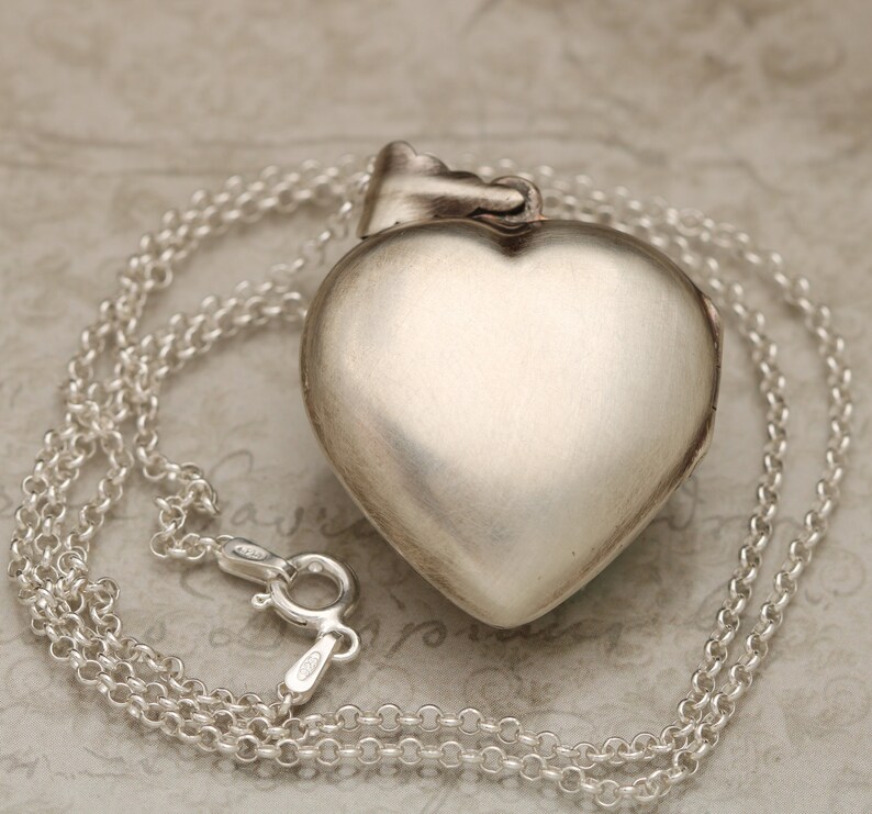 May include: A silver heart-shaped locket pendant with a chain. The locket is closed and has a smooth, polished finish.