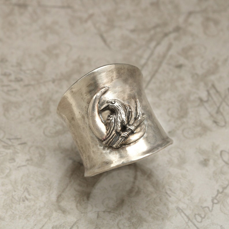 K&ouml;nnte beinhalten: Ein silberner Ring mit strukturierter Oberfl&auml;che zeigt ein erhabenes Design eines Vogels, der auf einem Halbmond sitzt.