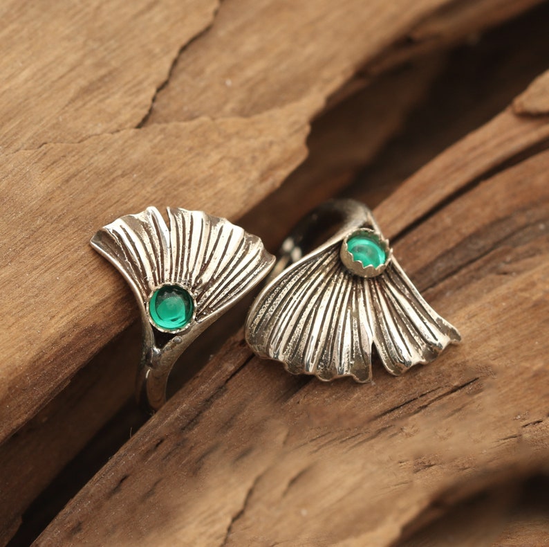 Puede incluir: Dos anillos de plata con detalles de piedras preciosas verdes. Los anillos tienen forma de hojas de ginkgo.