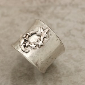 May include: A silver ring featuring a crescent moon and stars design. The ring is crafted from hammered metal and has a rustic appearance.