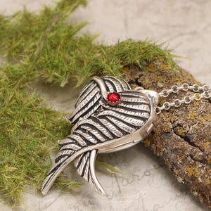 Pu&ograve; includere: Collana con ciondolo in argento a forma di cuore con ali dettagliate e un accento di pietra preziosa rossa.