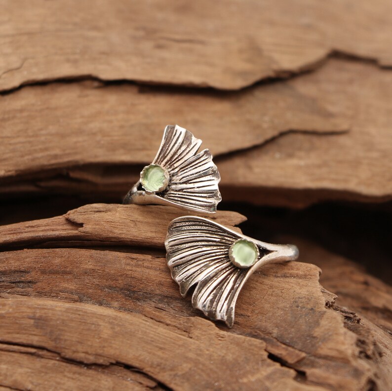 Puede incluir: Dos anillos de plata con un dise&ntilde;o de hoja de ginkgo y una piedra preciosa verde claro en el centro de cada hoja.
