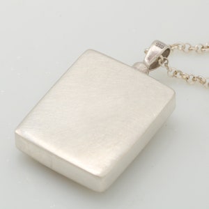 Op de afbeelding: Een zilveren hanger met een vierkante vorm en een gladde, geborstelde afwerking. De hanger is bevestigd aan een zilveren ketting met een karabijnhaak. De hanger is aan de achterkant gemarkeerd met het nummer "925".