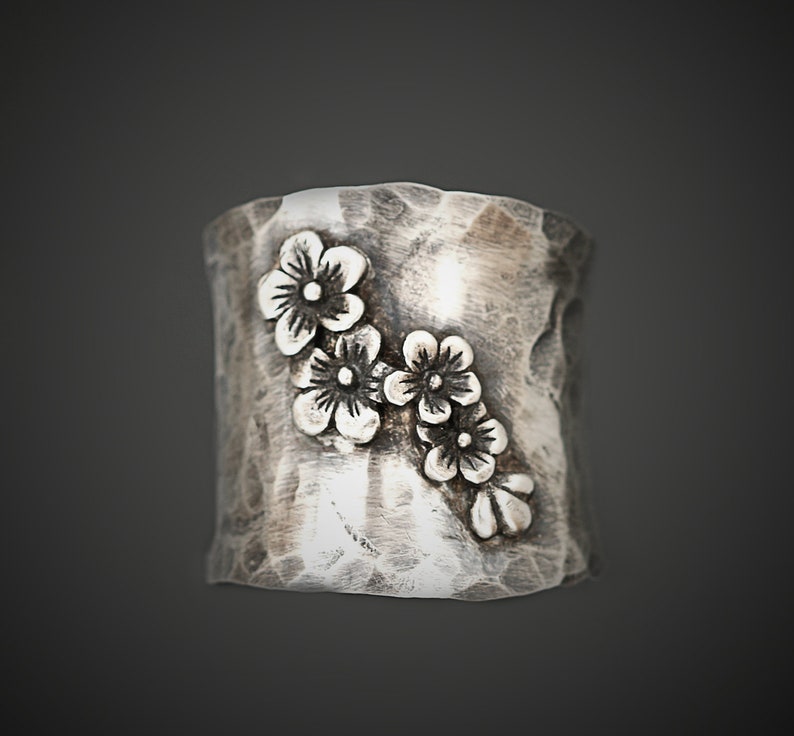 Puede incluir: Un anillo de plata con una superficie texturizada y un dise&ntilde;o de cinco peque&ntilde;as flores.