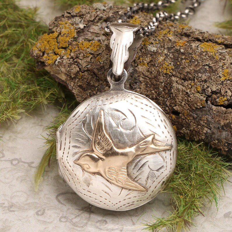 May include: Silver locket necklace with a gold bird design. The locket has a detailed engraved pattern and a delicate chain.