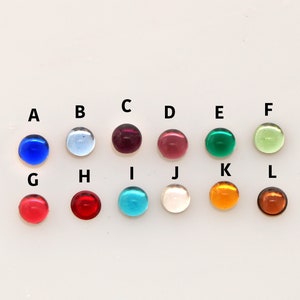 May include: Twelve small, round, smooth cabochon stones arranged in two rows of six. Each stone is labeled with a letter from A to L and features a distinct color, including shades of blue, red, green, yellow, orange, pink, and clear white.