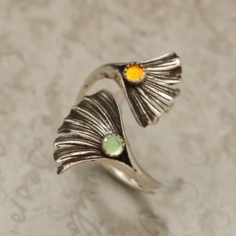 Puede incluir: Un anillo de plata con dos dise&ntilde;os de hojas de ginkgo. Las hojas est&aacute;n adornadas con una piedra preciosa amarilla y una piedra preciosa verde.