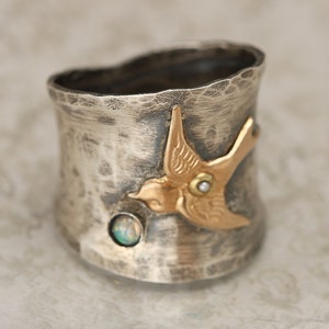 May include: A silver ring with a hammered finish features a gold bird with a pearl and opal accents.