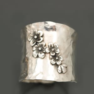 Puede incluir: Un anillo de plata con acabado martillado y un dise&ntilde;o de cinco flores delicadas.