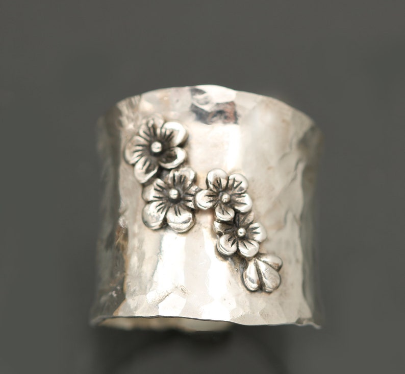 Puede incluir: Un anillo de plata con acabado martillado y un dise&ntilde;o de cinco flores delicadas.