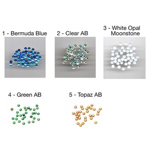 Pu&ograve; includere: Assortimento di piccole perline di vetro rotonde e iridescenti in vari colori, tra cui blu, verde, oro e bianco. Le perline sono disposte in gruppi di cinque, con ogni gruppo etichettato con un numero e un nome di colore. 1 - Blu delle Bermuda, 2 - Chiaro AB, 3 - Pietra lunare opale bianca, 4 - Verde AB, 5 - Topazio AB.