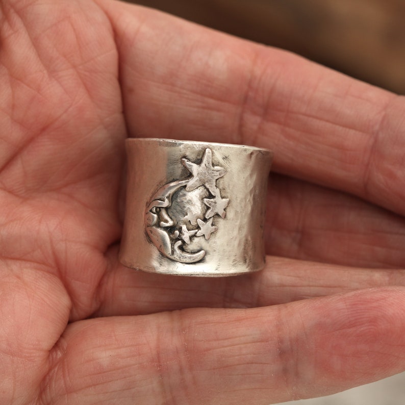 May include: A silver ring with a hammered finish and a design of a crescent moon and stars.