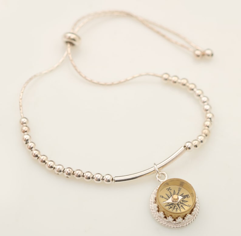 May include: A silver beaded bracelet with a compass charm. The bracelet has a sliding knot closure and is adjustable in size.
