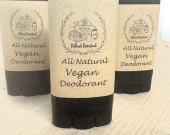 Puede incluir: Tres envases cilíndricos de desodorante. Los envases tienen una base y tapa negras, con una etiqueta de color beige. La etiqueta presenta un logotipo de escena de granja y las palabras "All Natural Vegan Deodorant". La marca "Holland Homestead" también es visible.