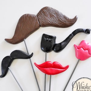 May include: Set of six colorful photo booth props, including a brown mustache, a black mustache, a black pipe, a red pair of lips, and two pink pairs of lips. The props are attached to wooden sticks.