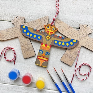 Könnte beinhalten: Holz-Totempfahl-Ornamente mit einem bemalten Design in Braun, Gelb, Blau und Orange. Das Bild enthält Farbtöpfe in Blau, Rot und Gelb sowie Pinsel und rot-weißes Garn.