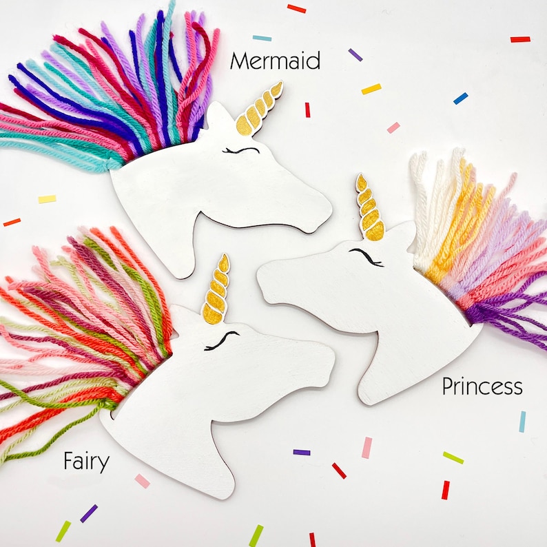 Puede incluir: Tres recortes de cabeza de unicornio blancos con crines de hilo colorido etiquetados como "Mermaid", "Fairy" y "Princess". Cada uno tiene un cuerno dorado y ojos cerrados. Formas de confeti de varios colores est&aacute;n dispersas.