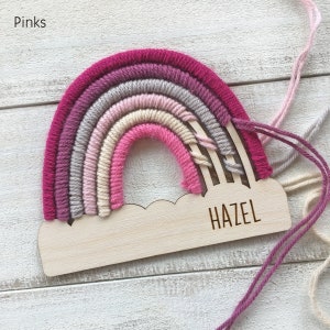 Pu&ograve; includere: Un'applique da parete a forma di arcobaleno fatta a mano nei toni del rosa, grigio e crema. L'arcobaleno &egrave; attaccato a una base di legno a forma di nuvola con il nome "HAZEL" inciso. La parola "Pinks" &egrave; nell'angolo in alto a sinistra.