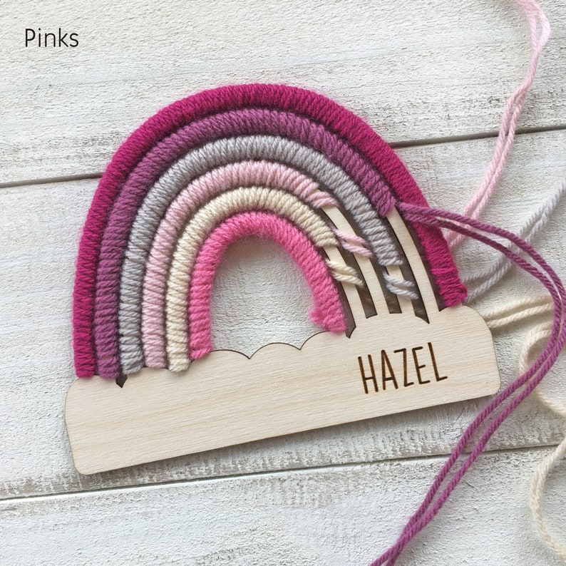 Pu&ograve; includere: Un'applique da parete a forma di arcobaleno fatta a mano nei toni del rosa, grigio e crema. L'arcobaleno &egrave; attaccato a una base di legno a forma di nuvola con il nome "HAZEL" inciso. La parola "Pinks" &egrave; nell'angolo in alto a sinistra.