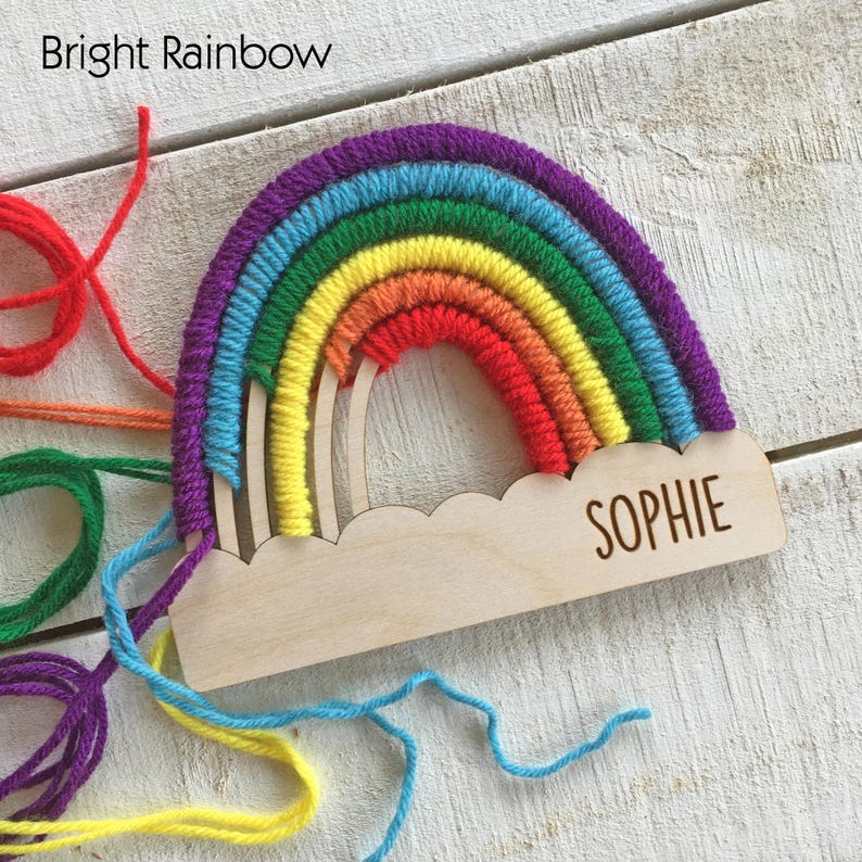 Pu&ograve; includere: Decorazione in legno a forma di arcobaleno con il nome "Sophie" inciso su una base a forma di nuvola. L'arcobaleno &egrave; realizzato con filato nei colori viola, blu, verde, giallo, arancione e rosso. Il testo "Bright Rainbow" &egrave; in alto.