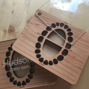 May include: Two wooden baby teeth charts with clear acrylic covers. The charts are labeled "Hudson baby teeth" and "Hailey baby teeth". Each chart has a grid for tracking the eruption of baby teeth, with sections for upper and lower teeth, and right and left sides.