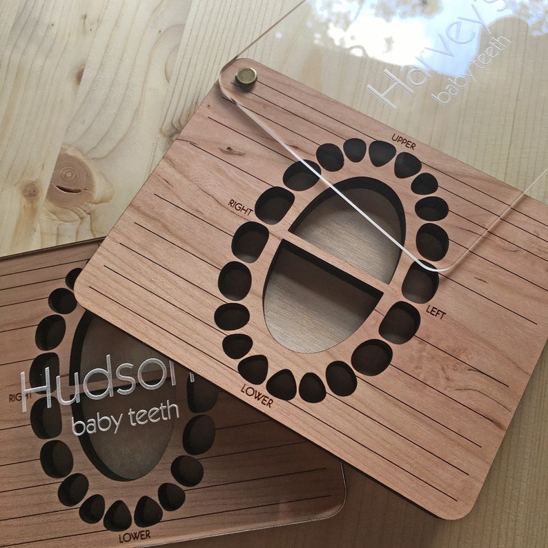 May include: Two wooden baby teeth charts with clear acrylic covers. The charts are labeled "Hudson baby teeth" and "Hailey baby teeth". Each chart has a grid for tracking the eruption of baby teeth, with sections for upper and lower teeth, and right and left sides.