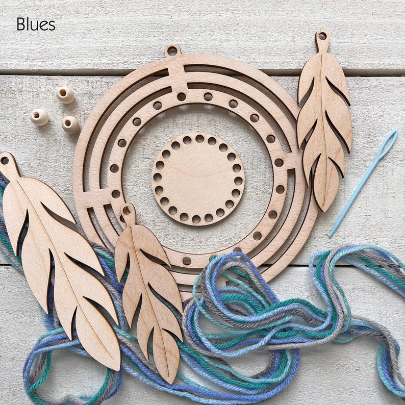 May include: A craft kit with wooden components for a dream catcher. The kit includes a circular frame, feather-shaped cutouts, wooden beads, and blue and gray yarn. A light blue needle is also included. The word "Blues" is in the upper left corner.