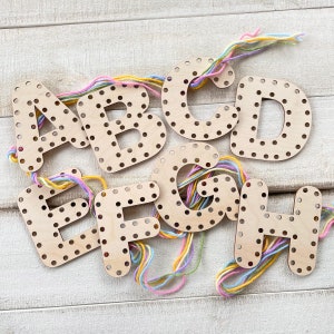 May include: Wooden letters A through H with holes for stringing. The letters are painted a light brown color and have a dotted pattern. Colorful yarn is wrapped around the letters.