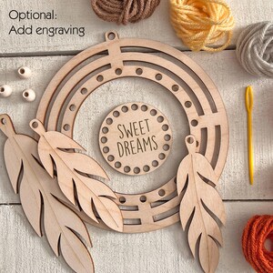 May include: A wooden dream catcher kit with a circular frame, feather cutouts, and a central disc that reads "SWEET DREAMS." The kit includes yarn in various colors and a yellow needle. The words "Optional: Add engraving" are also visible.