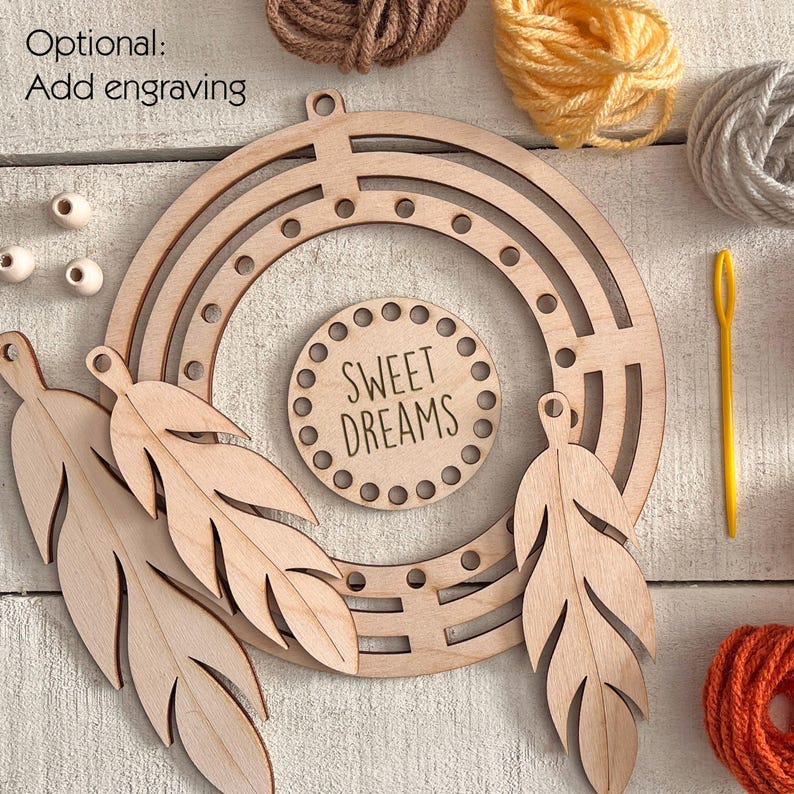 May include: A wooden dream catcher kit with a circular frame, feather cutouts, and a central disc that reads "SWEET DREAMS." The kit includes yarn in various colors and a yellow needle. The words "Optional: Add engraving" are also visible.