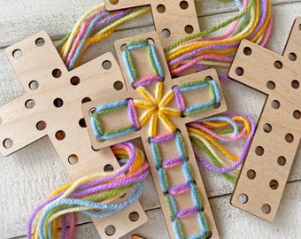 Puede incluir: Kit de manualidades en forma de cruz de madera con agujeros preperforados. La cruz está decorada con hilo colorido en tonos pastel de amarillo, verde, azul y rosa. Varias otras cruces de madera están dispersas.