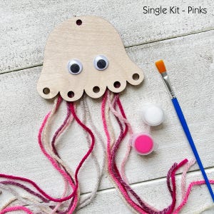 Puede incluir: Un kit de manualidades de medusas de madera con ojos saltones y tent&aacute;culos de hilo rosa, blanco y gris. Incluye botes de pintura y un pincel. El texto "Single Kit - Pinks" es visible.
