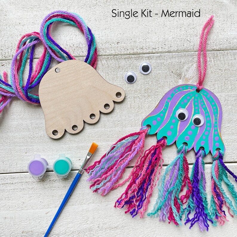 Puede incluir: Un kit de manualidades con tem&aacute;tica de sirenas con una forma de medusa de madera, pintura, hilo y ojos saltones. El kit incluye un pincel y dos botes de pintura peque&ntilde;os. El texto "Single Kit - Mermaid" es visible.