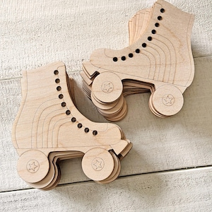 Puede incluir: Dos patines de ruedas de madera, cada uno con un diseño apilado. Los patines son de color marrón claro con detalles circulares negros para los ojales. Las ruedas son circulares con un diseño de estrella en el centro. Los patines están sobre una superficie de madera clara.