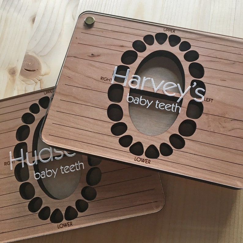 May include: Two wooden baby teeth keepsake boxes with a tooth chart design. The top box says "Harvey's baby teeth" and the bottom box says "Hudase baby teeth".