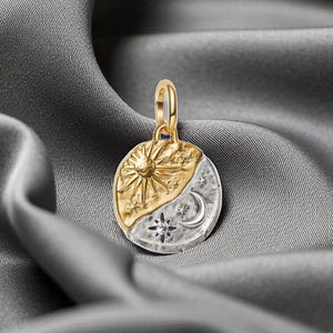 Può includere: Un ciondolo in oro e argento con un design celeste. Il ciondolo presenta un sole su una metà e una luna, stelle e un piccolo diamante sull'altra metà. Il ciondolo è appeso a un anello d'oro.