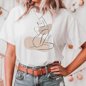 May include: White t-shirt with a line drawing of a woman in a seated pose. The drawing is in brown and beige tones. The text "BOHEMIAN" is printed on the shirt.