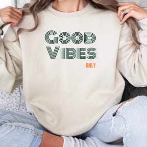 May include: A cream colored sweatshirt with the text "GOOD VIBES ONLY" in green and orange lettering.