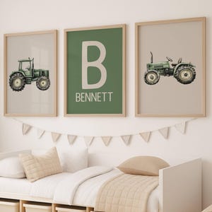 Könnte beinhalten: Drei gerahmte Drucke mit einem Bauernhof-Thema. Zwei Drucke zeigen grüne Traktoren auf neutralen Hintergründen. Der mittlere Druck hat einen großen weißen Buchstaben "B" und den Namen "BENNETT" auf grünem Hintergrund. Die Drucke befinden sich über einem Bett.