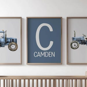 May include: Three framed prints featuring a blue tractor illustration and a blue print with the name "Camden". The tractor art has a watercolor style with a light blue color scheme. The frames are a light brown color.