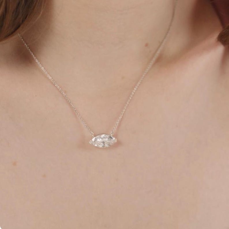 May include: A delicate silver necklace featuring a marquise-cut gemstone pendant. The pendant is the focal point, showcasing a clear, sparkling stone. The necklace is simple and elegant, suitable for everyday wear or special occasions.